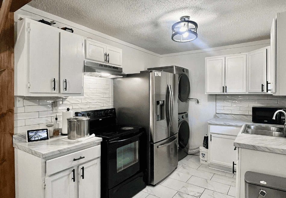 Modern white kitchen featuring stainless steel appliances, subway tile backsplash, and stacked laundry machines.